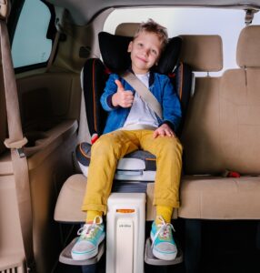 Dziecko w foteliku samochodowym z poprawnie zmiętymi pasami i podnóżkiem do fotelika dla dziecka